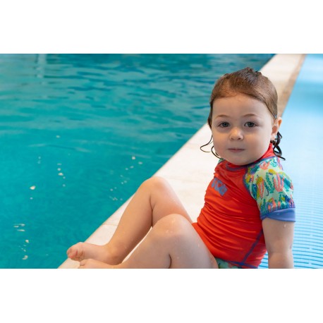 Criança sentada na borda da piscina com camisola de proteção solar