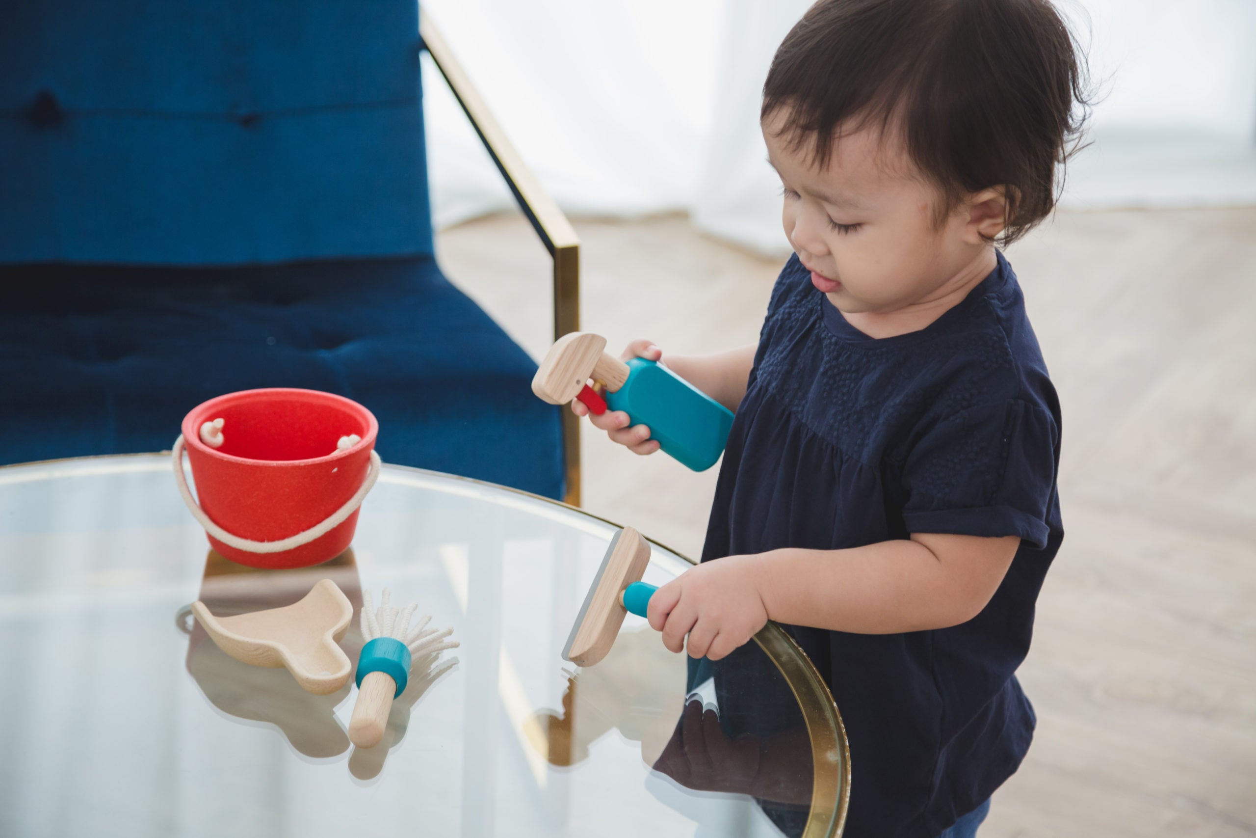 Criança a brincar com o conjunto de limpeza PlanToys sobre uma mesa.