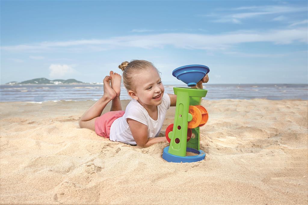 Criança a brincar com o moinho de areia e água da Hape na praia.