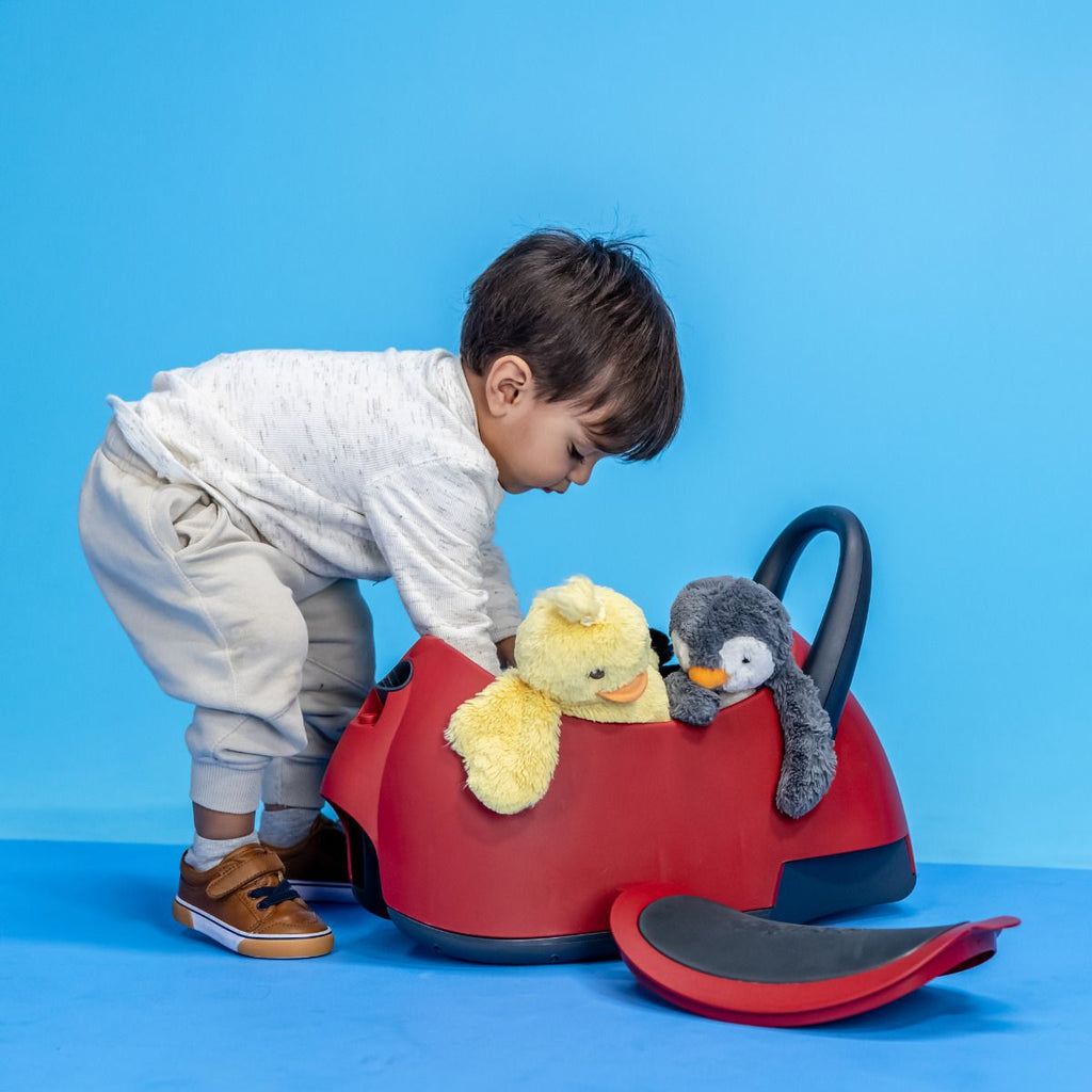 Criança a colocar dois peluches (pato e pinguim) no compartimento de arrumação do Glider Luna, que está no modo veículo de passeio.