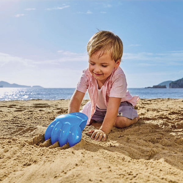 Criança sorridente a usar a pá escavadora azul Hape na praia