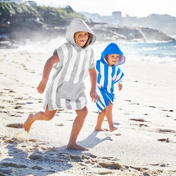 Duas crianças a correr na areia da praia vestindo ponchos de secagem rapida.