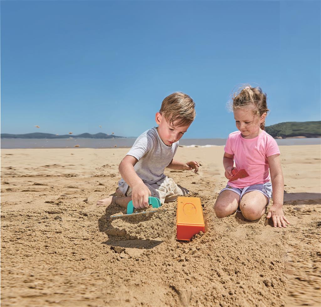 Duas crianças a brincar na praia a construir um castelo de areia com ferramentas Hape.