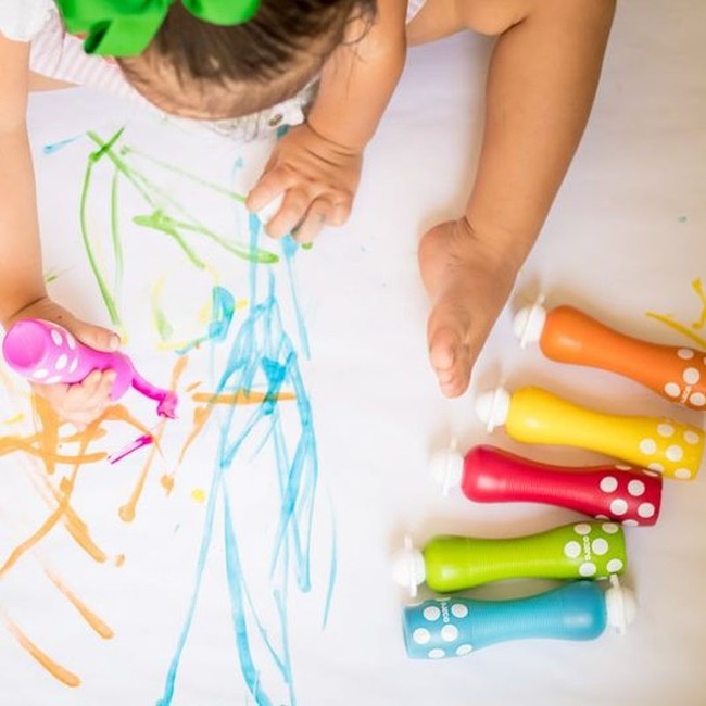 Criança pequena a desenhar com um marcador rosa Djeco de ponta de esponja, enquanto os outros marcadores estão dispostos ao lado.