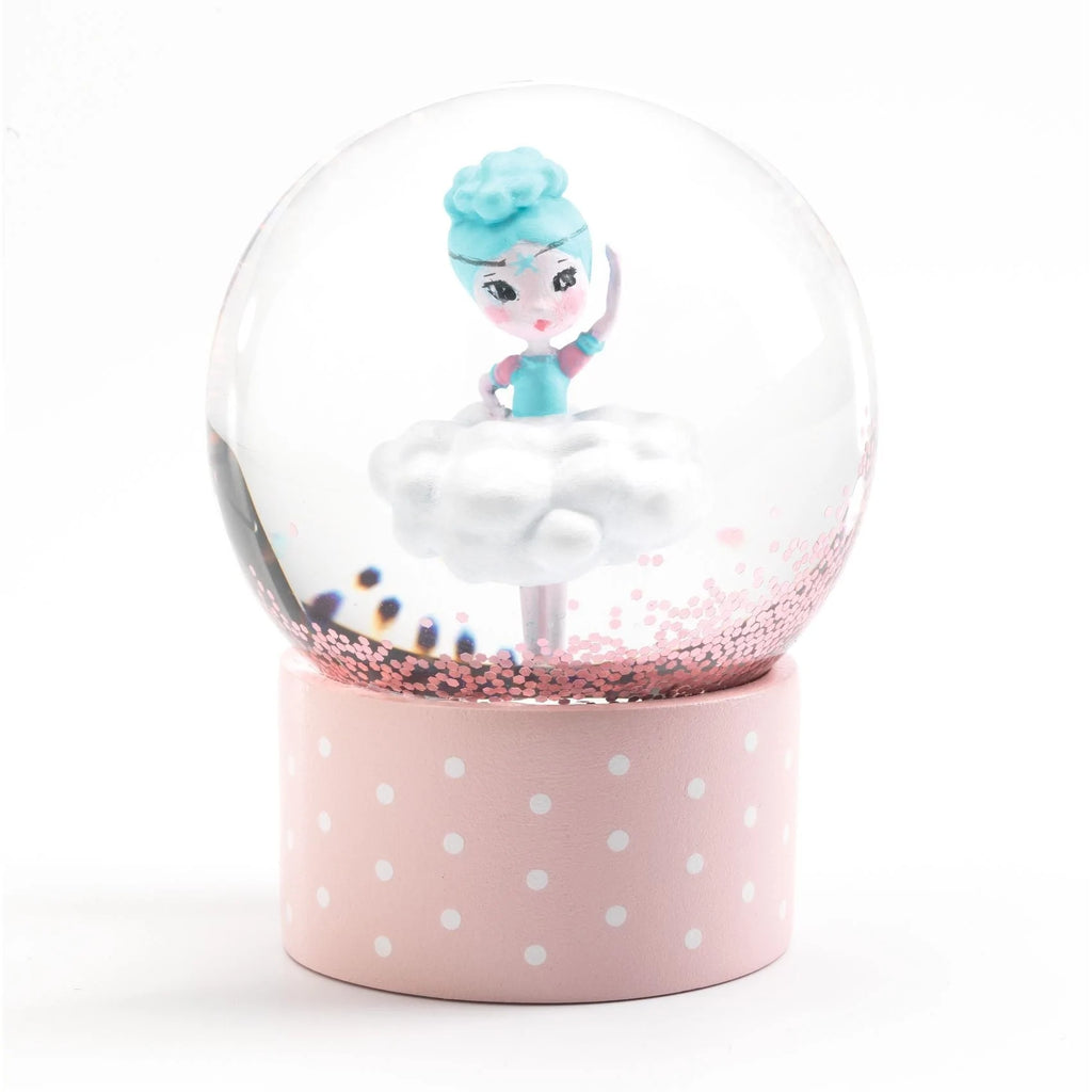 Close-up do mini globo de neve Djeco com uma bailarina em cima de uma nuvem, sobre base rosa com bolinhas brancas.