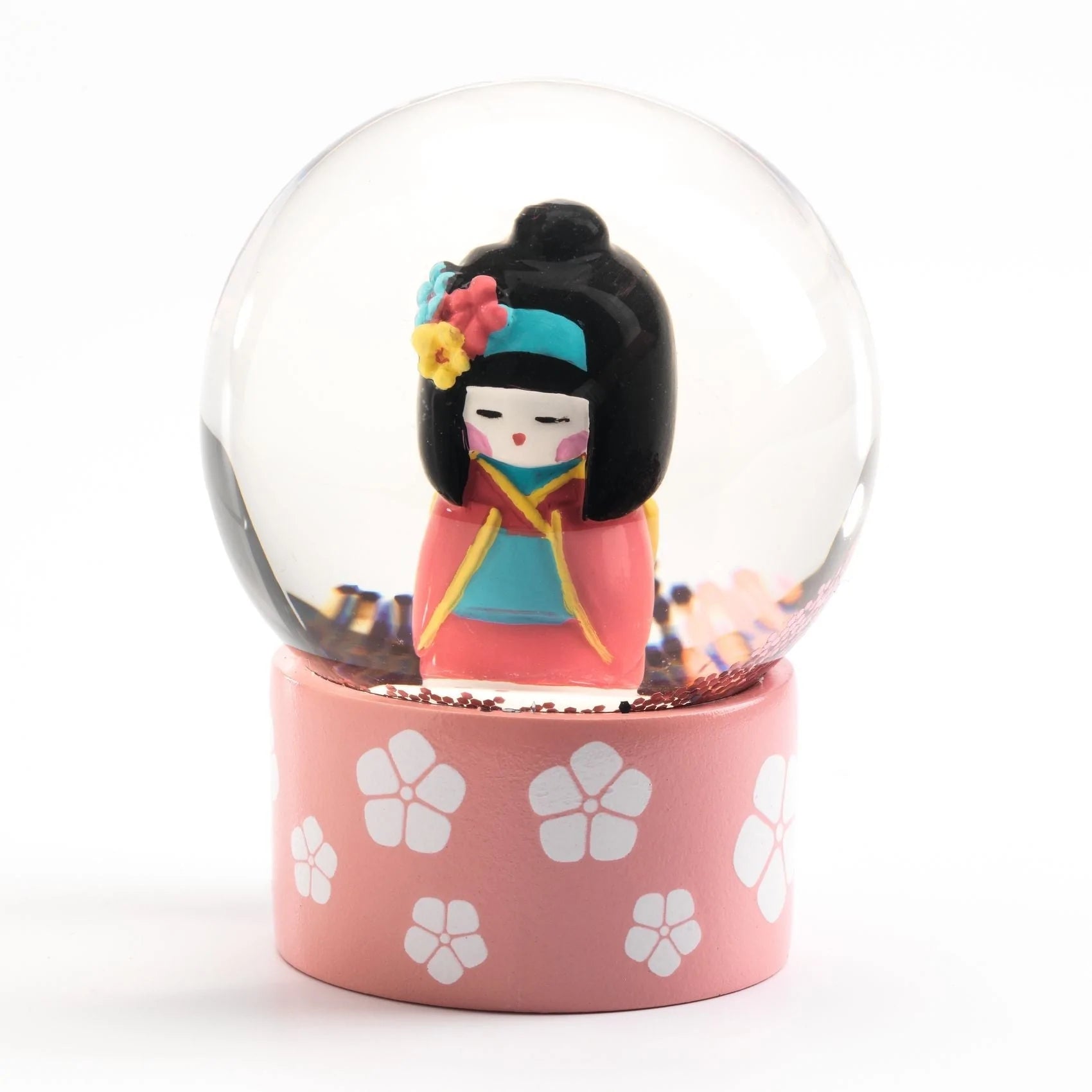 Detalhe do mini globo de neve Djeco com a figura de uma boneca Kokeshi japonesa em traje rosa e preto, sobre base decorada.