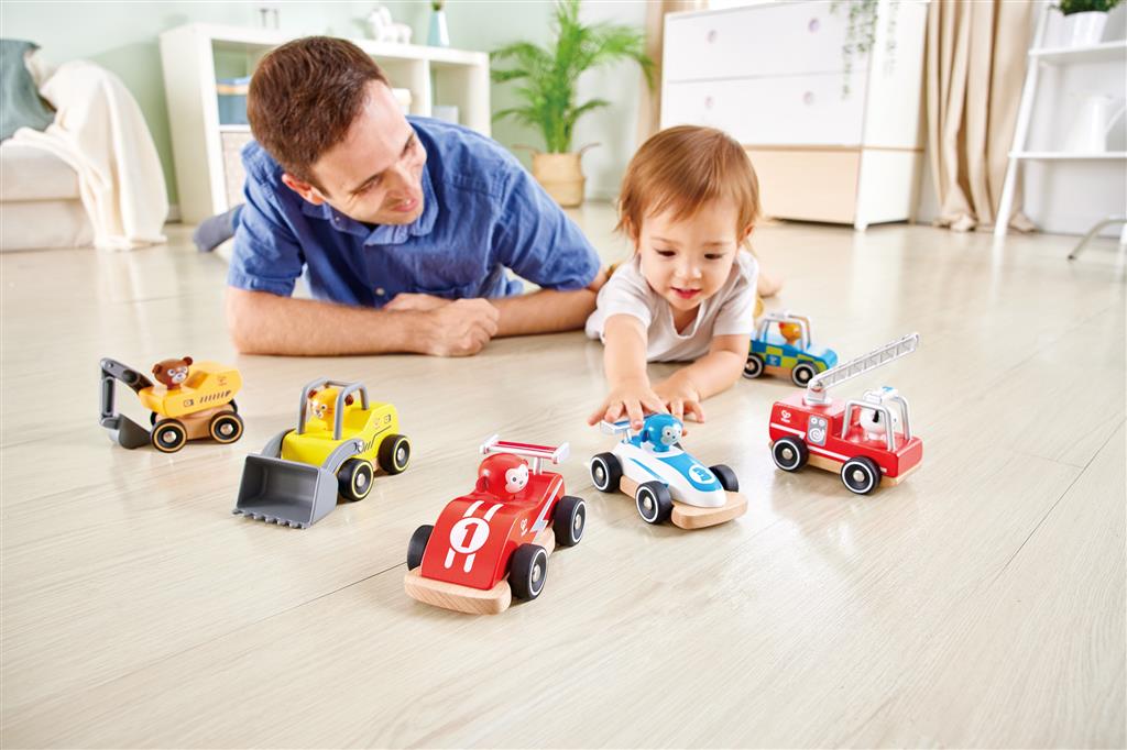 Pai e filho a brincar no chão com a coleção de Hape Carrinhos Sortidos, demonstrando a diversão e interação do brinquedo.