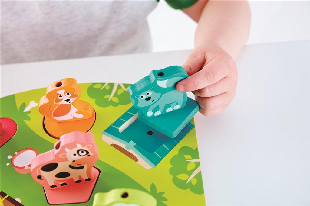 Detalhe da mão de uma criança a encaixar uma peça de animal azul no Hape Puzzle encaixável e sonoro A Quinta.