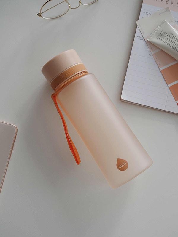 A garrafa Equa Tritan Sunrise Laranja 600ml em ambiente de utilização, ideal para ginásio ou exterior, destacando a portabilidade.