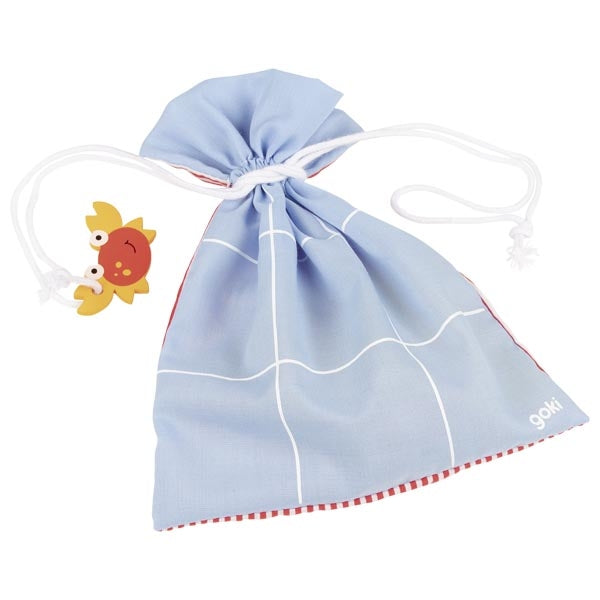 Saco de tecido azul com o padrão de tabuleiro de jogo desenhado a branco, fechado com cordão, com uma peça de caranguejo de madeira pendurada.