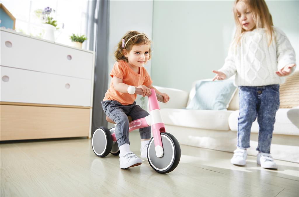 Criança a brincar com a bicicleta de equilíbrio Hape A minha primeira Vespa Rosa em casa, promovendo a atividade física e o desenvolvimento motor.