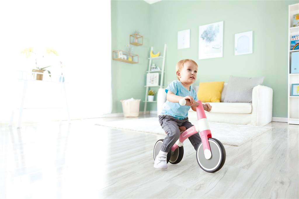 Criança pequena a andar na bicicleta de equilíbrio Hape A minha primeira Vespa Rosa em casa, desenvolvendo o equilíbrio e a coordenação.