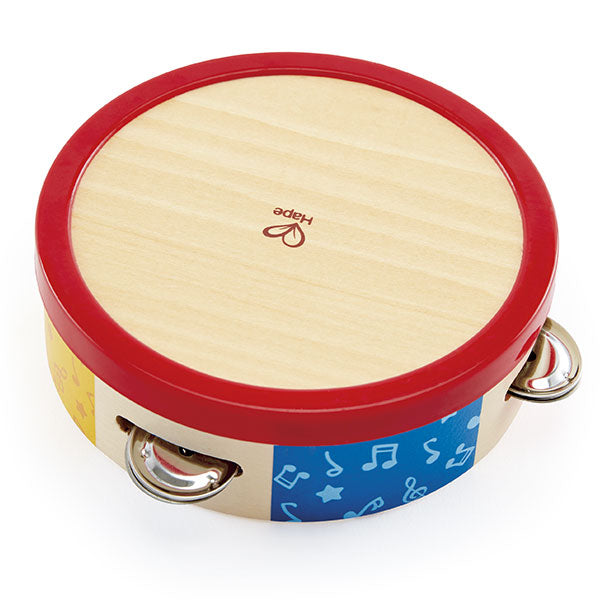 Detalhe da mão de uma criança a tocar a pandeireta Hape, mostrando a interação e os sinos a vibrar.