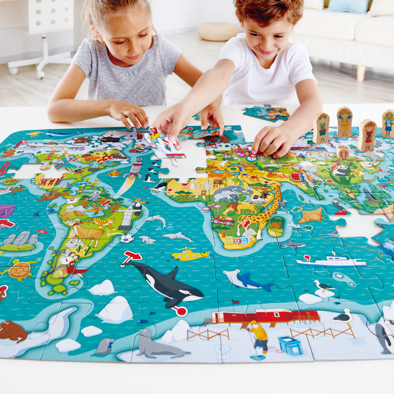 Detalhe do puzzle Hape com peças de madeira de viajantes (peões) posicionadas sobre o mapa do mundo.