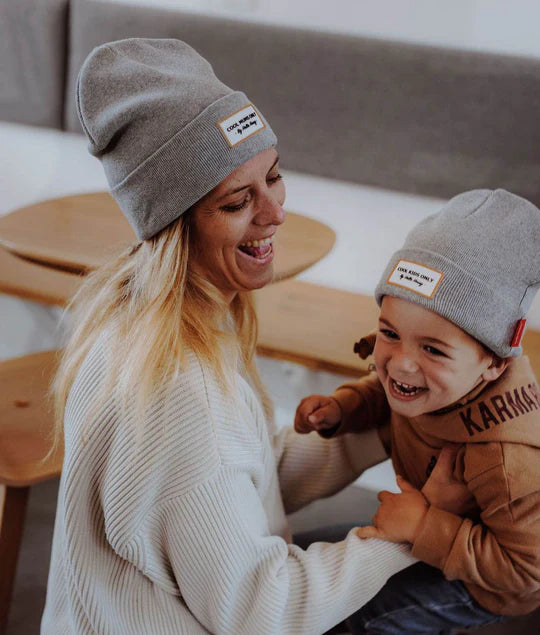 Mãe e filho a rir, ambos com gorro cinzento Hello Hossy. Mostra gorro criança em uso e etiqueta.