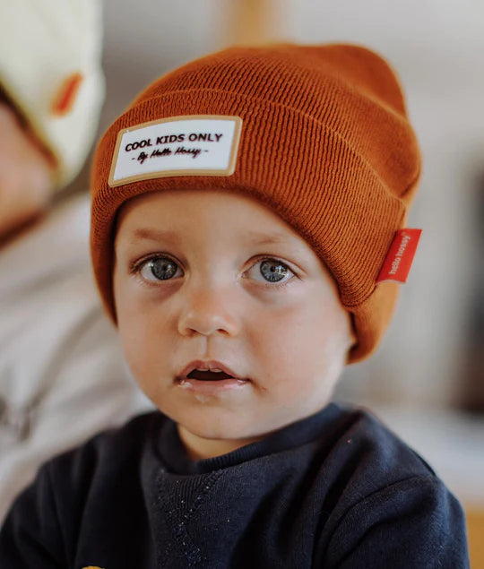 Close-up de criança a usar gorro laranja Hello Hossy. Mostra o gorro em uso e a etiqueta "COOL KIDS ONLY".
