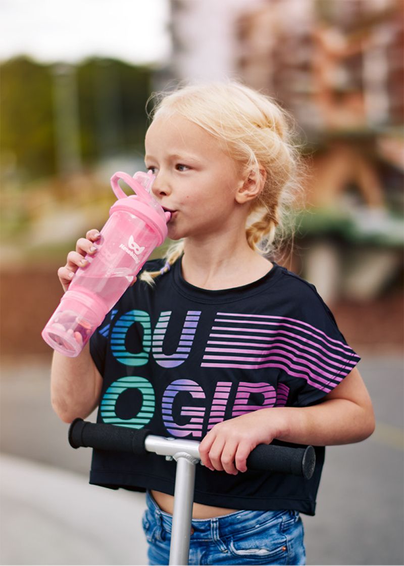 Criança a beber água de um copo Herobility Sport enquanto segura numa trotinete.