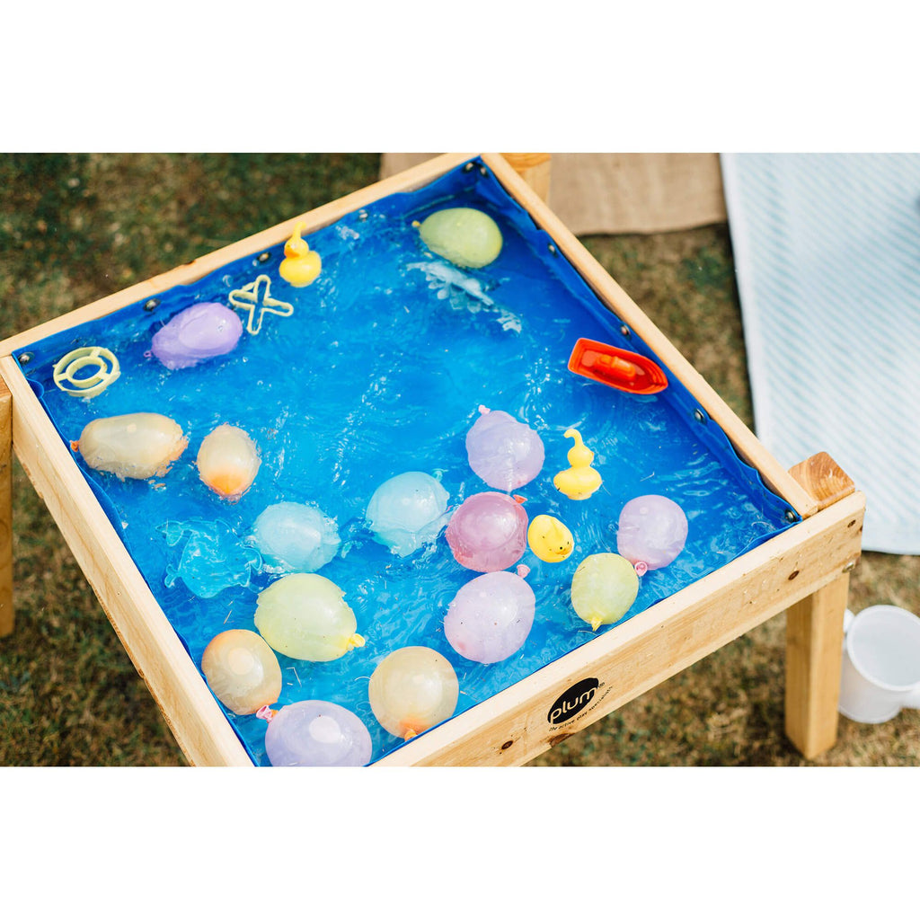 Vista aérea da mesa Plum multiusos para ar livre, com o forro azul cheio de água, balões e pequenos brinquedos flutuantes.