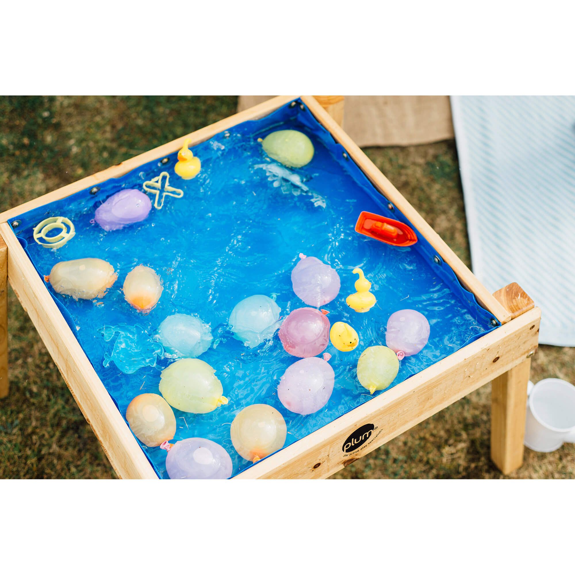 Vista aérea da mesa Plum multiusos para ar livre, com o forro azul cheio de água, balões e pequenos brinquedos flutuantes.