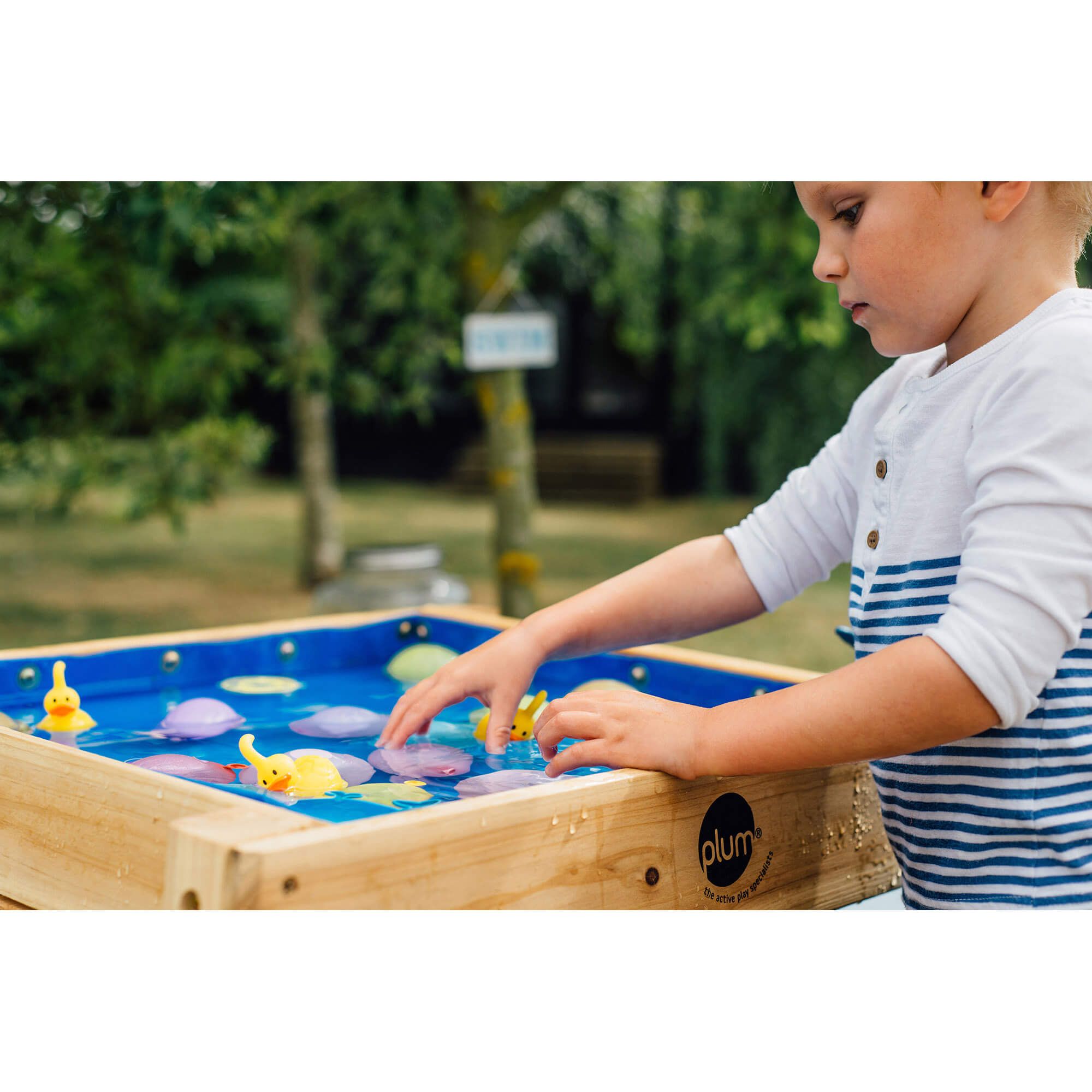 Criança a brincar com patinhos e nenúfares na mesa de água Plum multiusos para ar livre, num jardim.