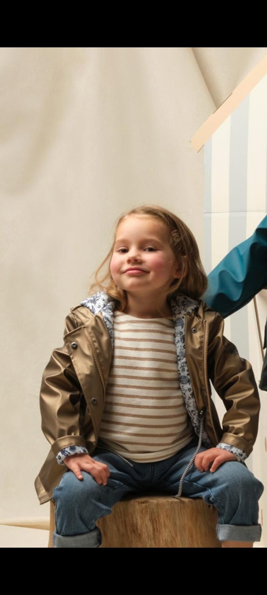 Casaco impermeável Hublot dourado metalizado para criança, visto de frente, com capuz e fecho de molas visível. Foco no acabamento brilhante.