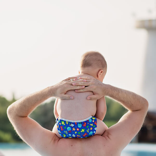 Bebé com fralda de natação ImseVimse ao colo dos pais junto à piscina.