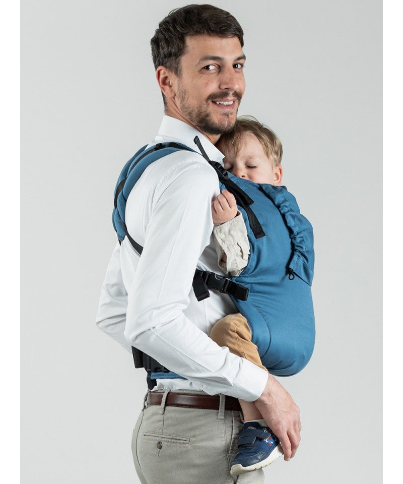 Homem usando a Mochila Isara Toddler Preschooler BLUESTONE, carregando um bebé.