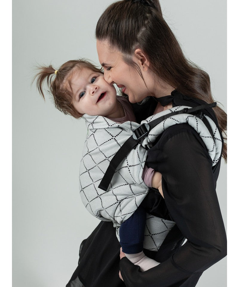 Mãe sorridente carregando um bebé na mochila Isara Toddler Preschooler DIAMONDA GREY, em posição frontal.