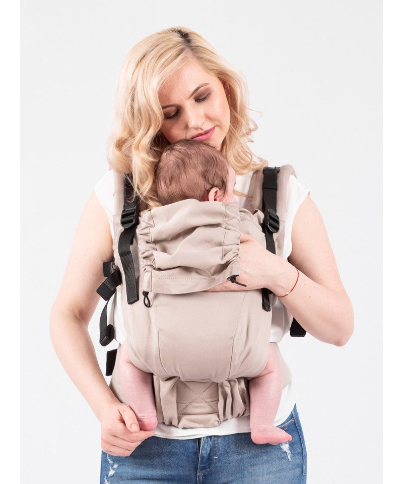 Mulher loira a sorrir com um bebé na frente, usando a Mochila Isara THE One Ajustável CAFFE LATTE.