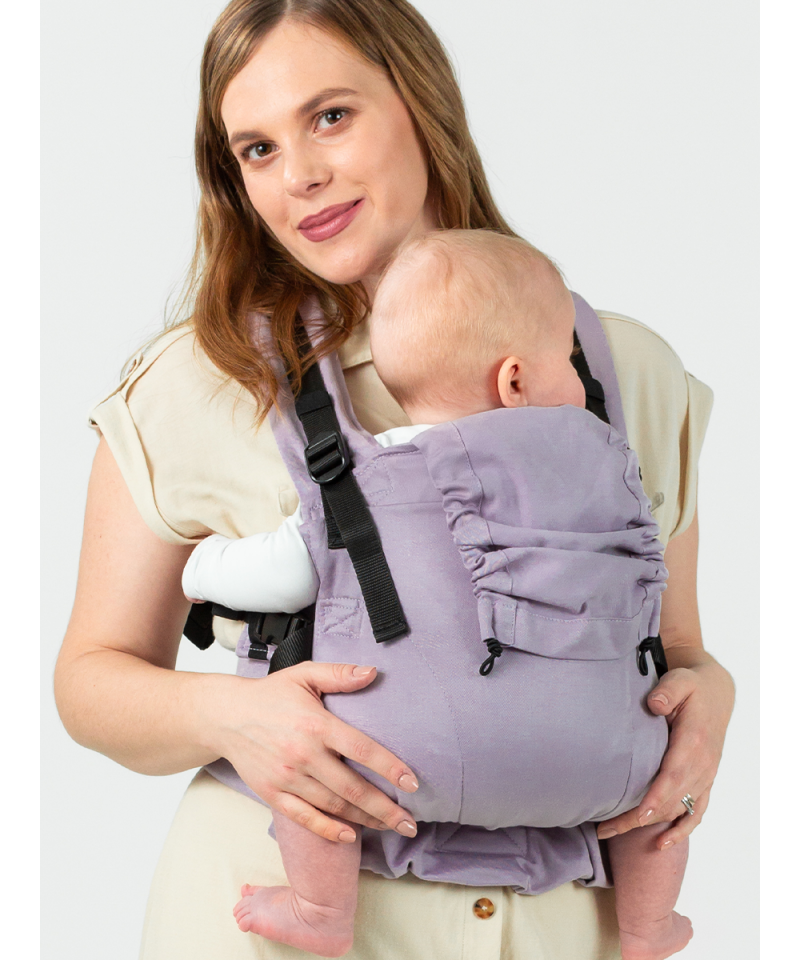 Mulher a usar a Mochila Isara THE One Ajustável LAVENDER, carregando um bebé na frente, com um sorriso suave. O bebé está confortavelmente ajustado e seguro.