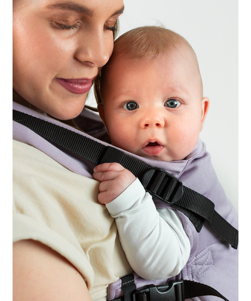 Mulher a usar a Mochila Isara THE One Ajustável LAVENDER, carregando um bebé na frente, com um sorriso suave. O bebé está confortavelmente ajustado e seguro.