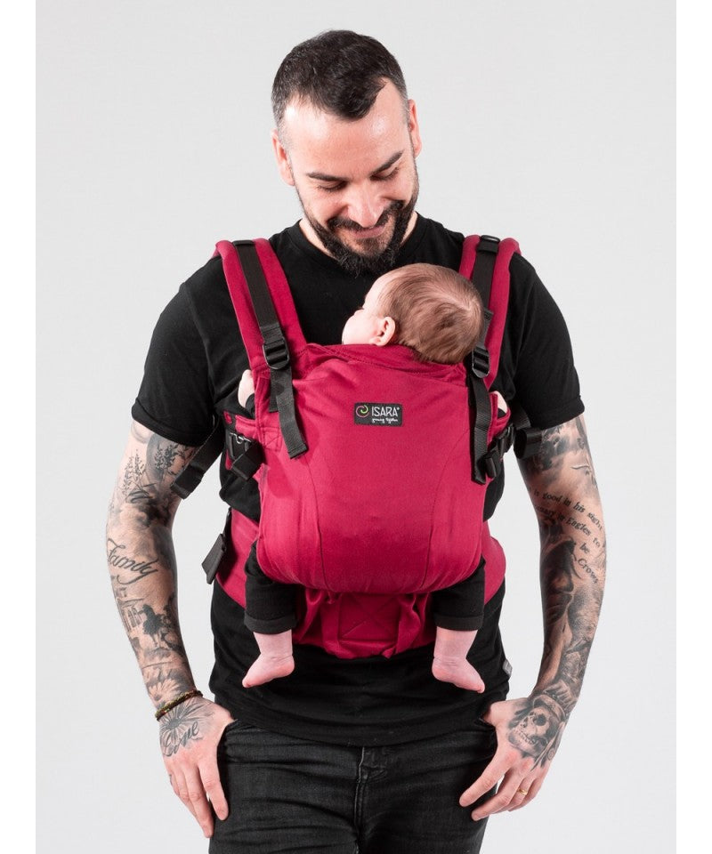 Pai com tatuagens olhando para baixo enquanto carrega bebé num porta-bebés vermelho ISARA The ONE, foco no painel frontal.