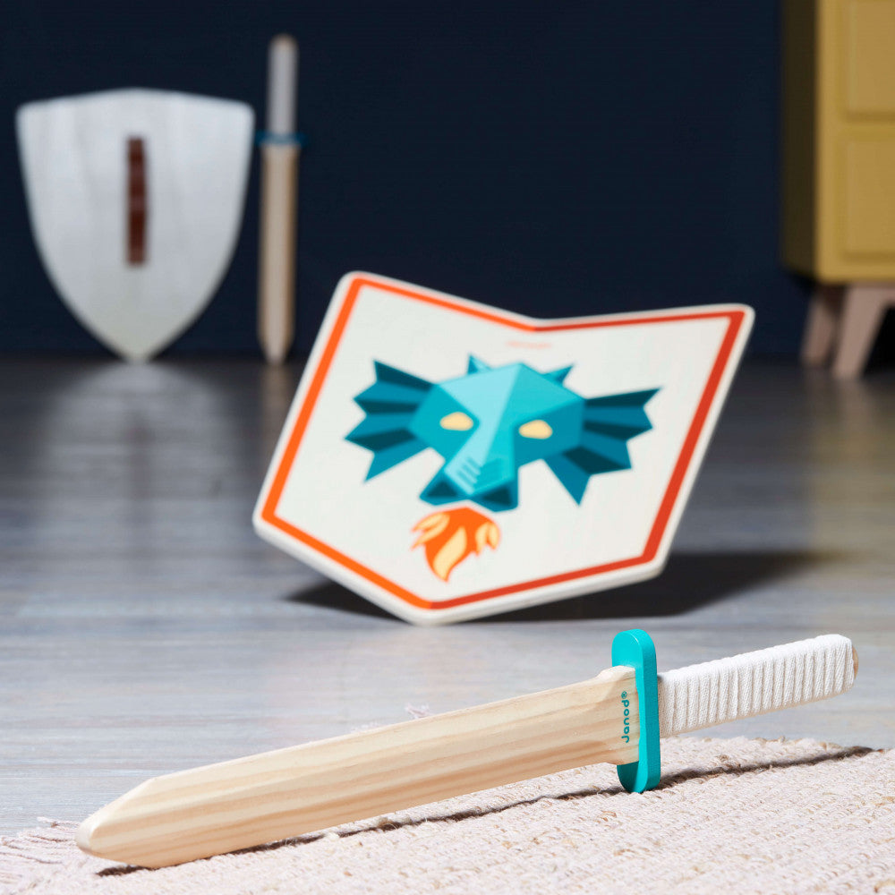 Conjunto Janod de escudo e espada de madeira com design de dragão em destaque num cenário de brincadeira.