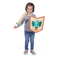 Menina a segurar o conjunto Janod de escudo e espada de madeira Dragão, sorridente e pronta para jogar.