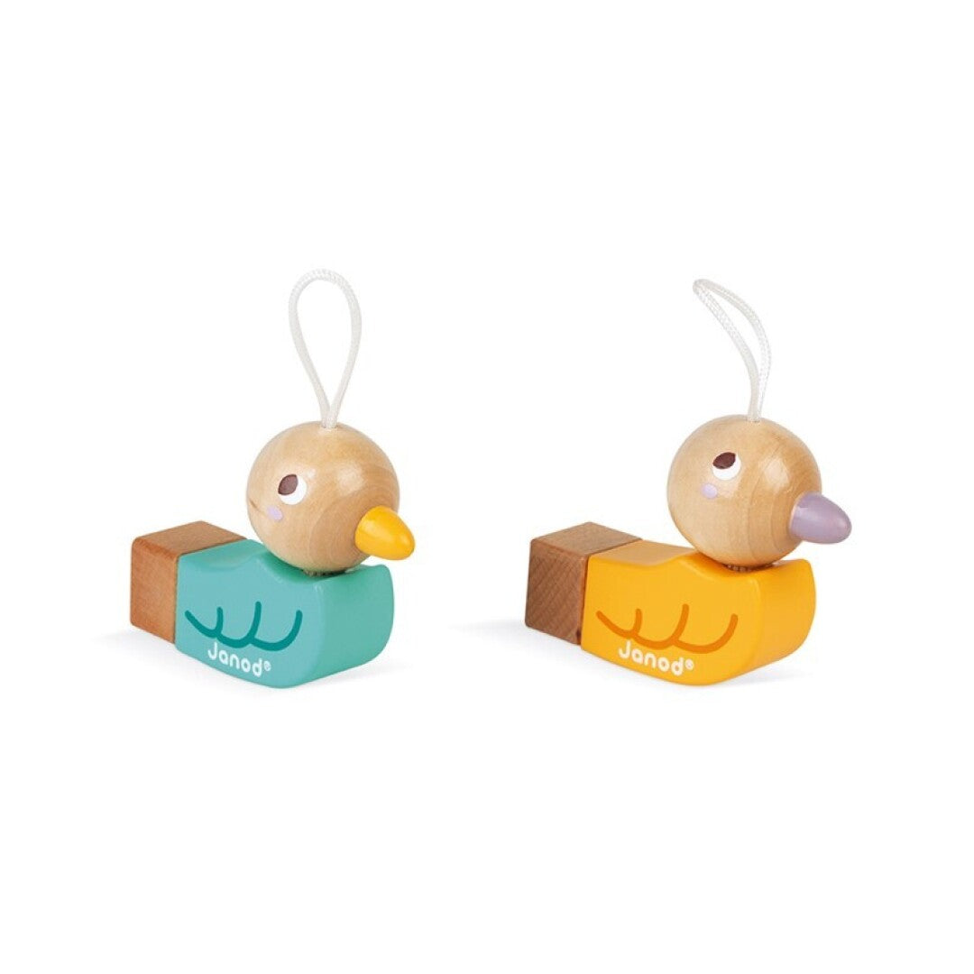 Dois patinhos apito de madeira Janod, um amarelo e um verde, lado a lado, prontos para serem pendurados. Fundo branco.