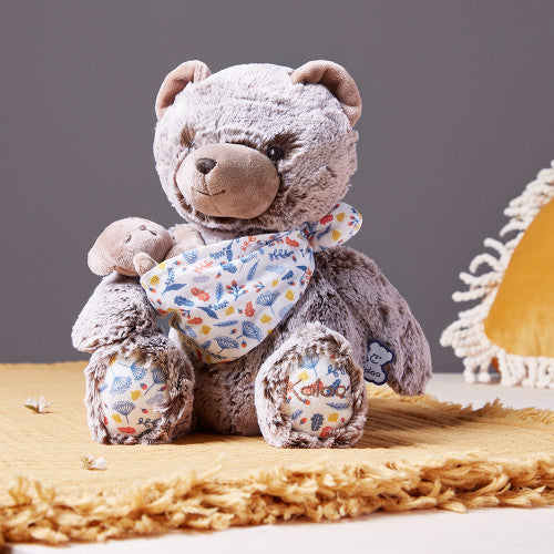 Vista lateral do peluche Kaloo, destacando o urso pai de 35cm a usar o porta-bebés com estampa.