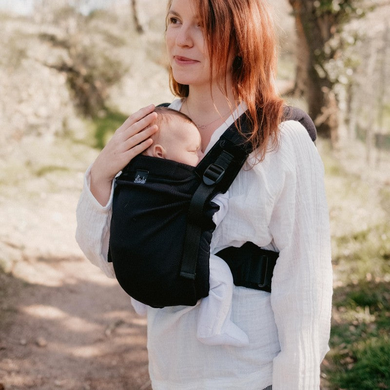 Mulher a utilizar a Mochila Neobulle MyNeo em um ambiente exterior, carregando um bebé na posição frontal.