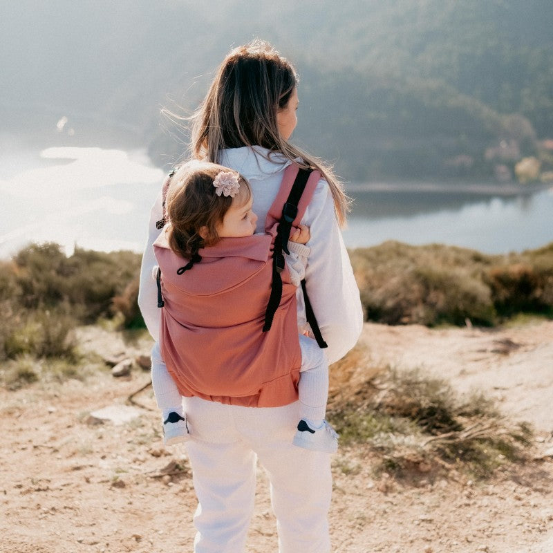 Vista traseira de uma mãe a usar a Mochila Neobulle Néo+ enquanto caminha ao ar livre.