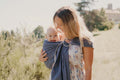 Mãe a caminhar ao ar livre com o seu bebé no sling de argolas Neobulle Bleu Cobalt, evidenciando a praticidade do produto.