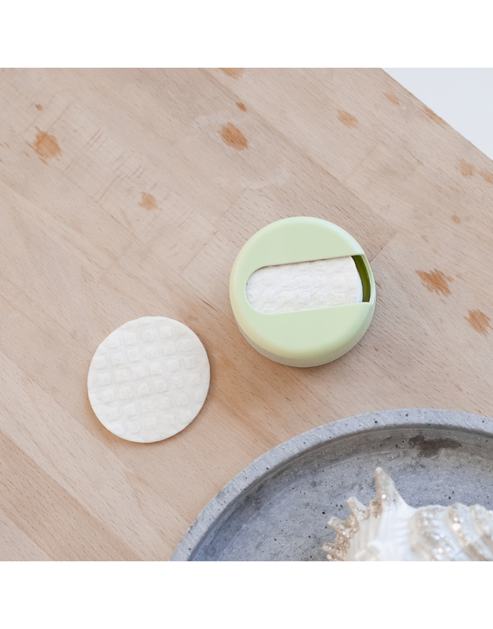 Imagem lifestyle mostrando uma mão a segurar um disco LastRound, pronto para remover maquilhagem, num ambiente de casa de banho minimalista.