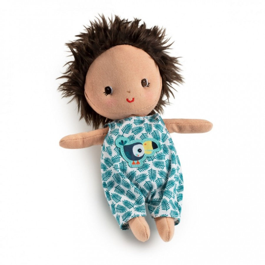 Boneca de peluche "Ari" da Lilliputiens, com pele escura, cabelo castanho despenteado e um macacão estampado com tucano e folhas verdes.