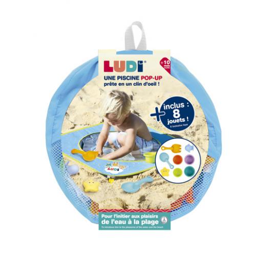 Piscina de praia pop-up Ludi montada na areia, com água, mostrando o sistema de fixação e o design compacto para bebés.
