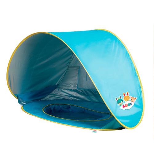 Tenda piscina Ludi Pop Up azul e cinzenta montada na praia, com criança a brincar na água perto da areia.