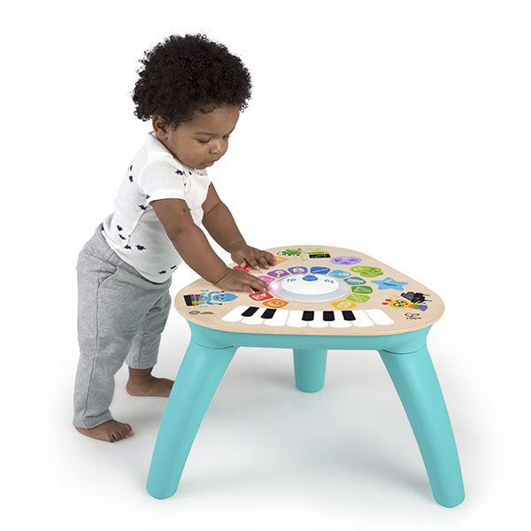 Bebé a brincar de pé com a Hape Baby Einstein Mesa de Atividades Magic Touch, tocando nas teclas e ícones coloridos.