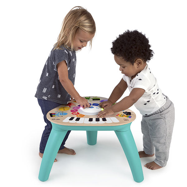 Duas crianças, uma de pé e outra mais nova, a brincar juntas na Hape Baby Einstein Mesa de Atividades Magic Touch, explorando os sons.
