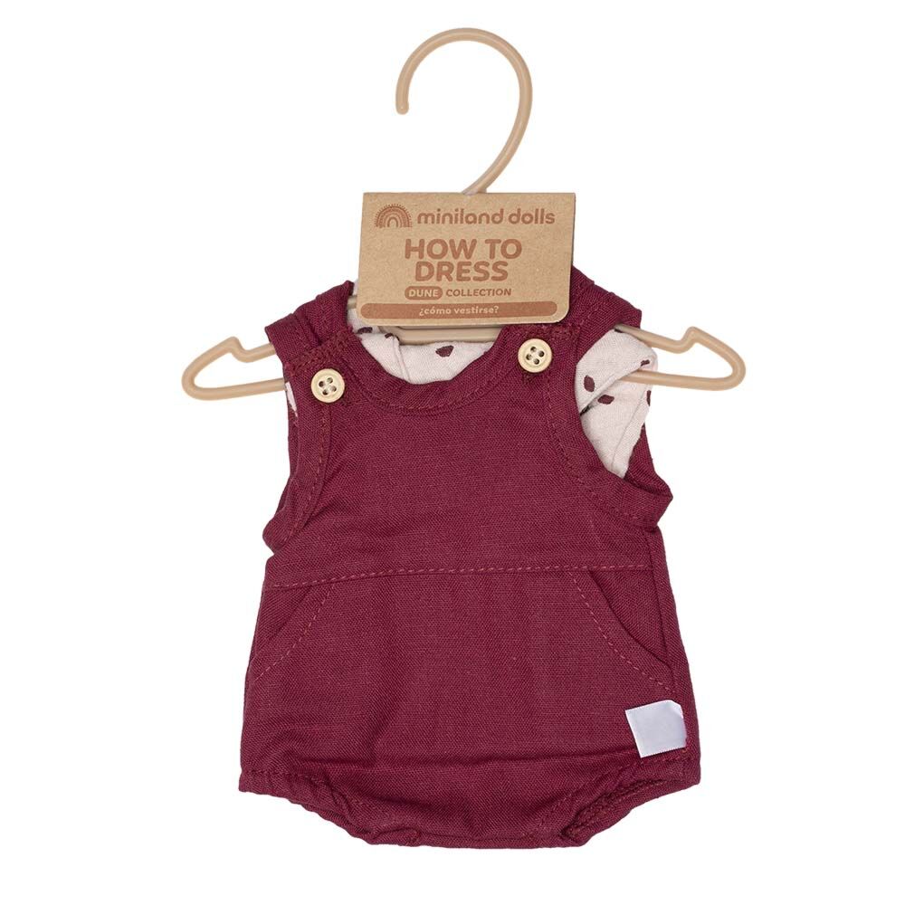 Roupa de boneca Miniland com o macacão bordeaux pendurado num cabide de plástico bege, com etiqueta de instruções "How to Dress".