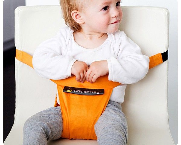 Bebé com arnês Minimonkey laranja numa cadeira