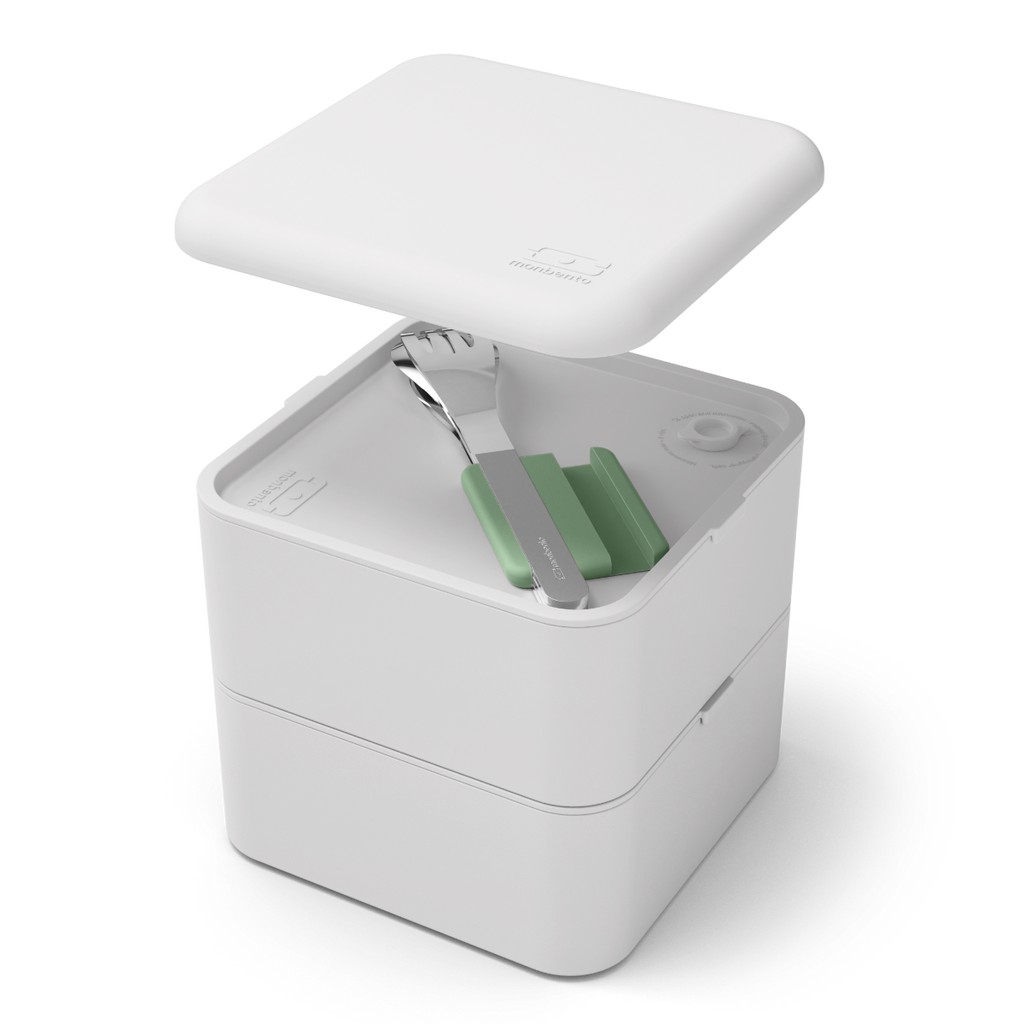 Vista superior de um conjunto de talheres Monbento em aço inox com suporte verde, inseridos num recipiente de almoço (bento box) branco.