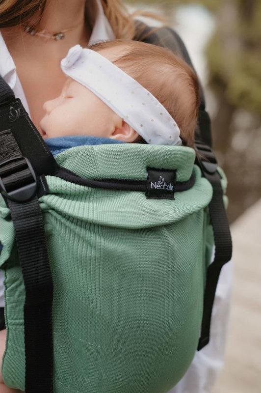 Mulher carregando um bebé numa mochila Neobulle MyNeo Vert, com foco no bebé adormecido e no conforto da mochila.