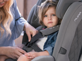 Criança sentada na cadeira auto Nuna Myti enquanto um adulto ajusta o arnês.